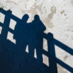 shadows of two people on a beach boardwalk